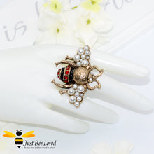 Load image into Gallery viewer, A decorative bee-shaped ring with red rhinestone crystals and white pearls, in aged gold colour.