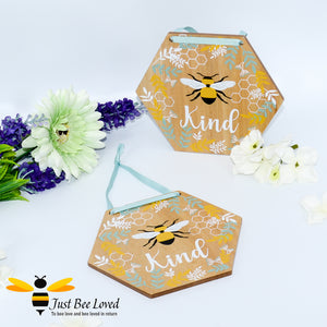 hexagon shaped wooden hanging plaque with a pictorial message "Bee Kind", decorated with painted honeycomb, blue & white leaves with matching blue hanging ribbon.