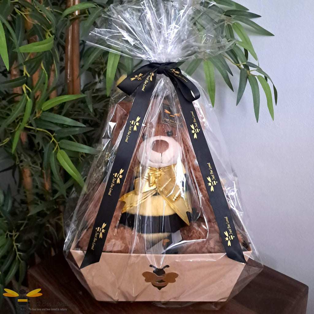 Bee themed hamper gift box with a plush bee bear toy inside, wrapped in clear cellophane with a black and gold ribbon bow.