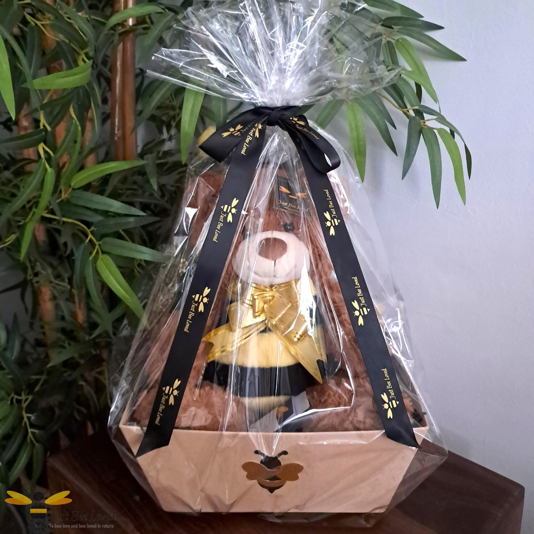 Bee themed hamper gift box with a plush bee bear toy inside, wrapped in clear cellophane with a black and gold ribbon bow.