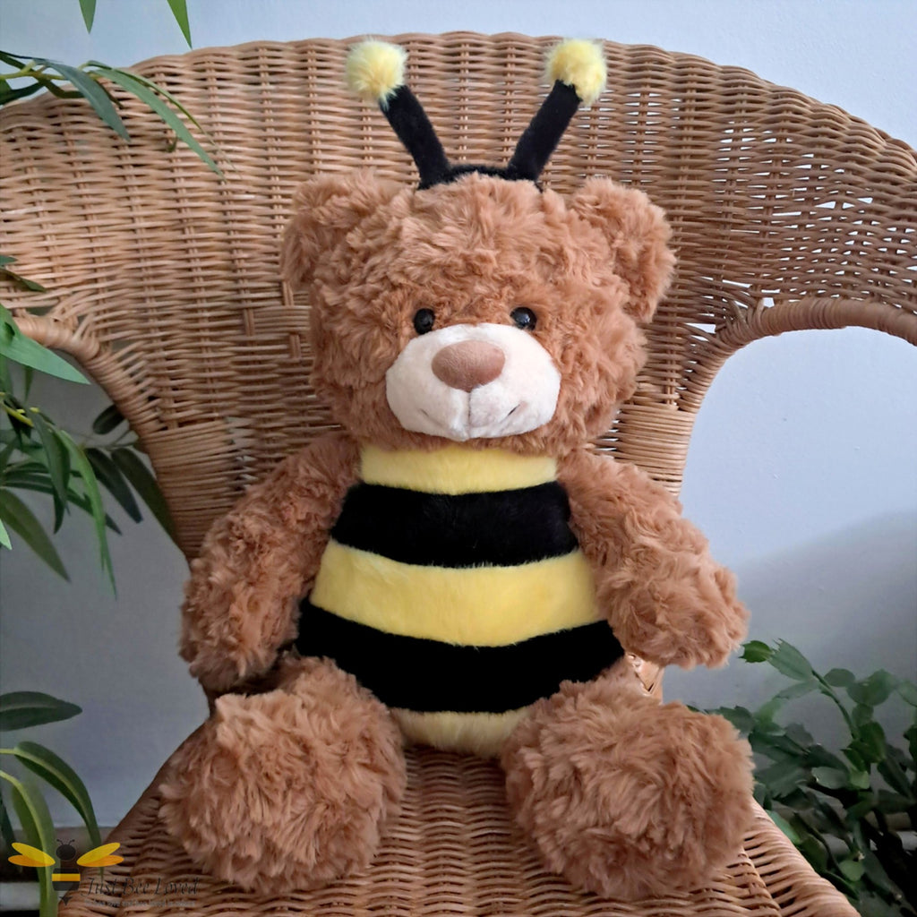 a brown plush shaggy teddy bear dressed as a bee with antennae sitting on a wicker chair.