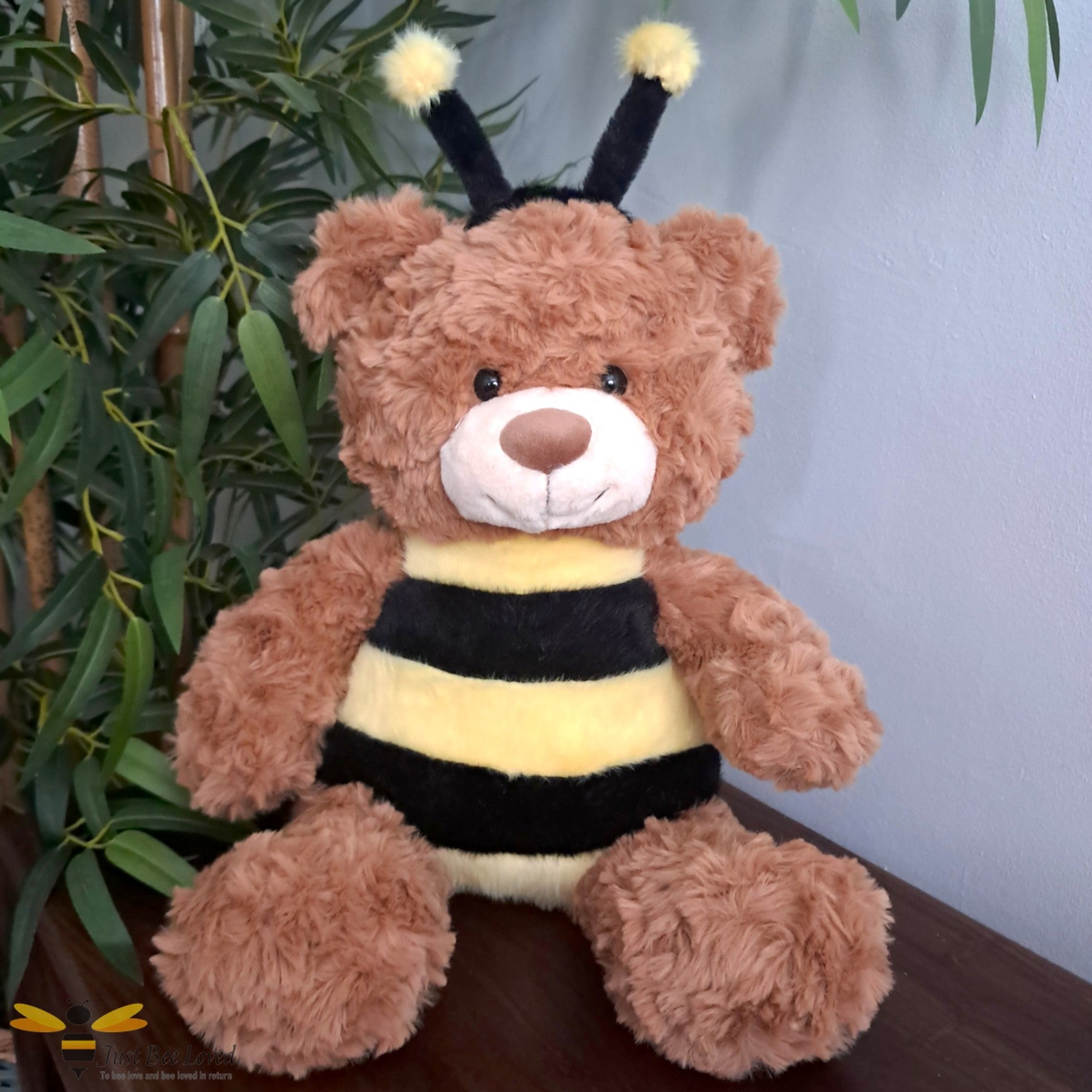 A brown shaggy teddy bear dressed as a bee with antennae head-piece.