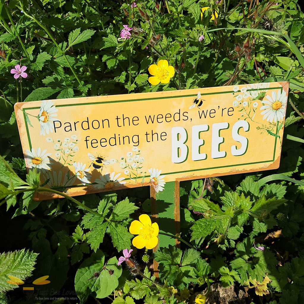 Garden metal sign with text 'Pardon the weeds, we're feeding the bees'.