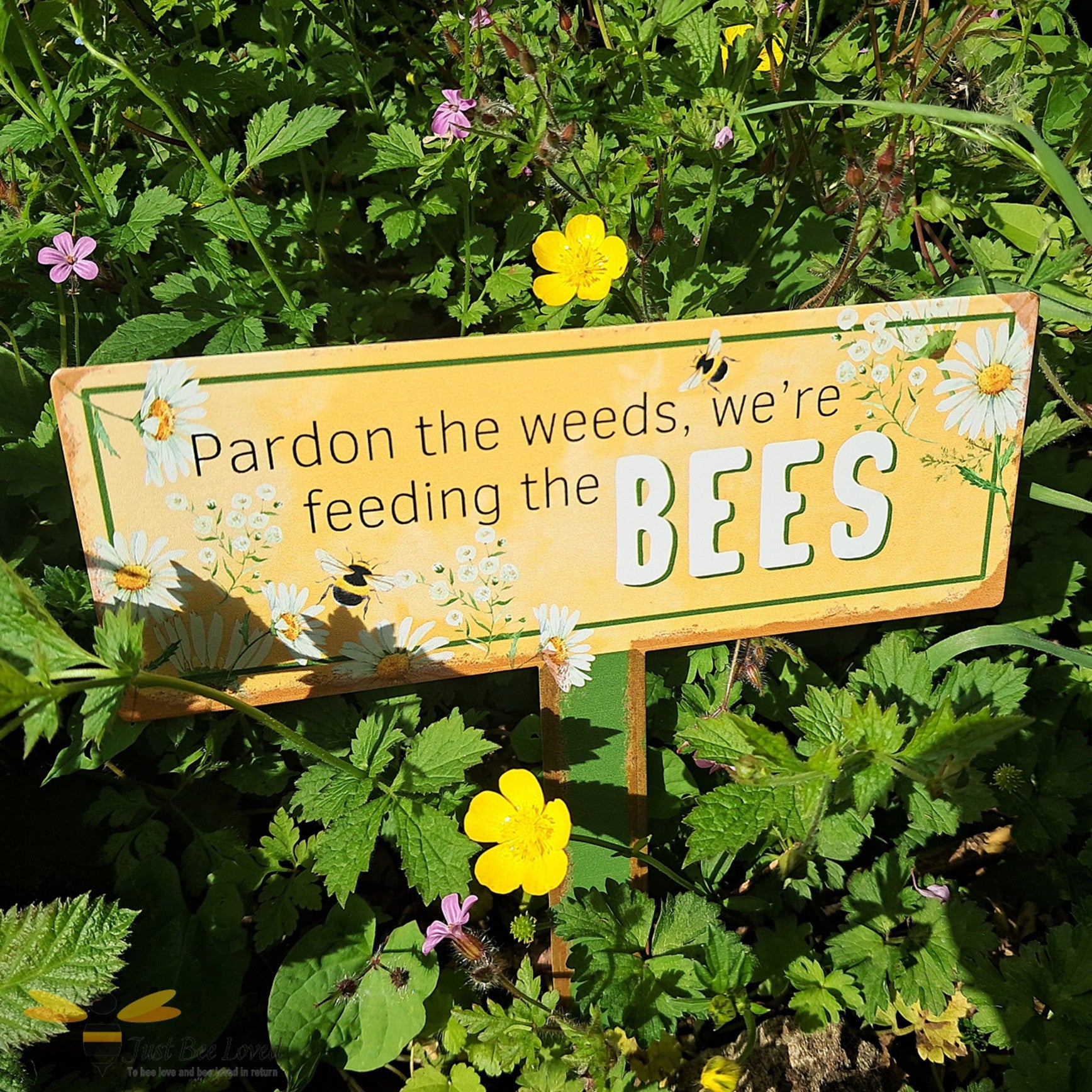 Garden metal sign with text 'Pardon the weeds, we're feeding the bees'.