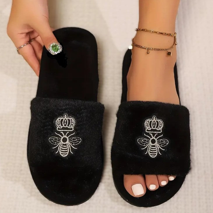 A pair of black plush slippers with a embroidered crowned queen bee motif.