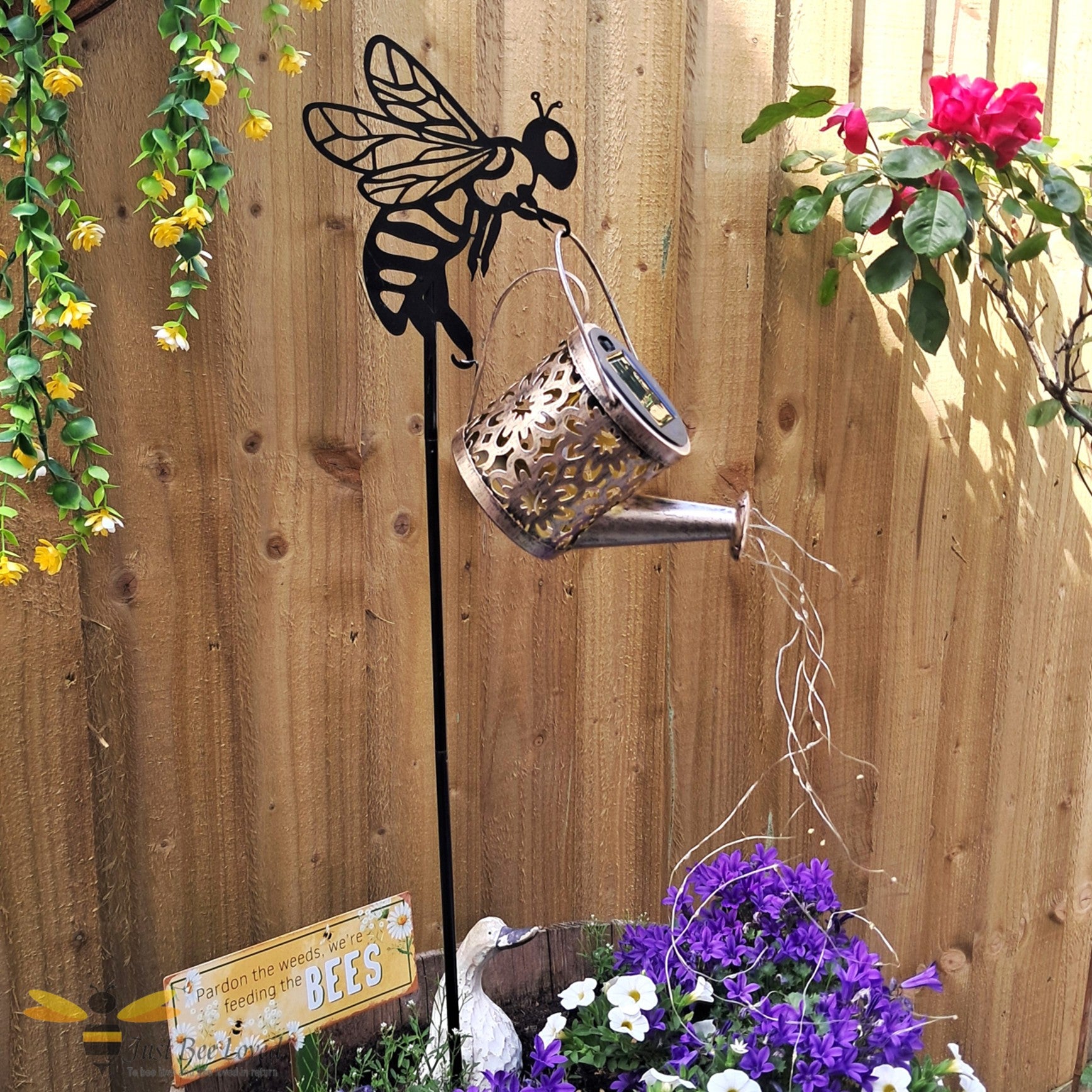 Metal garden stake shaped like a bee with a solar light watering can feature and cascading string lights.
