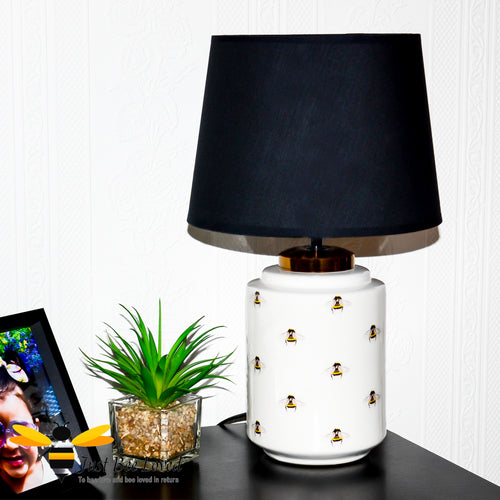 white ceramic table lamp features an all over pattern of bumble bees with black cotton shade