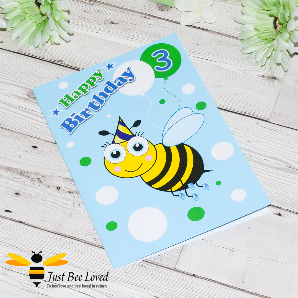 A blue greeting card with a cartoon bee illustration, featuring 'Happy Birthday' text with colourful balloons and the number 3.