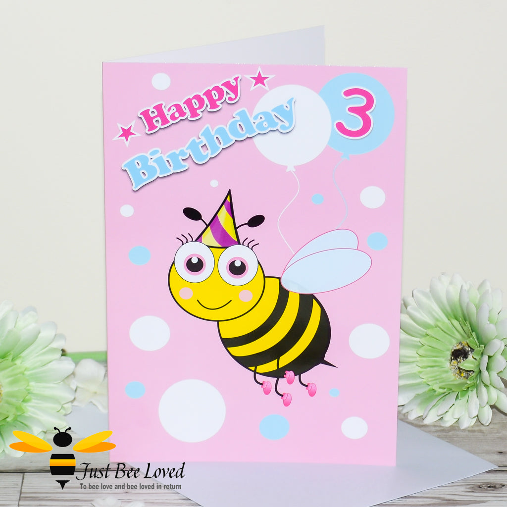 a pink birthday greeting card for girl featuring a cartoon bee wearing a party hat, with balloons and the number 3.