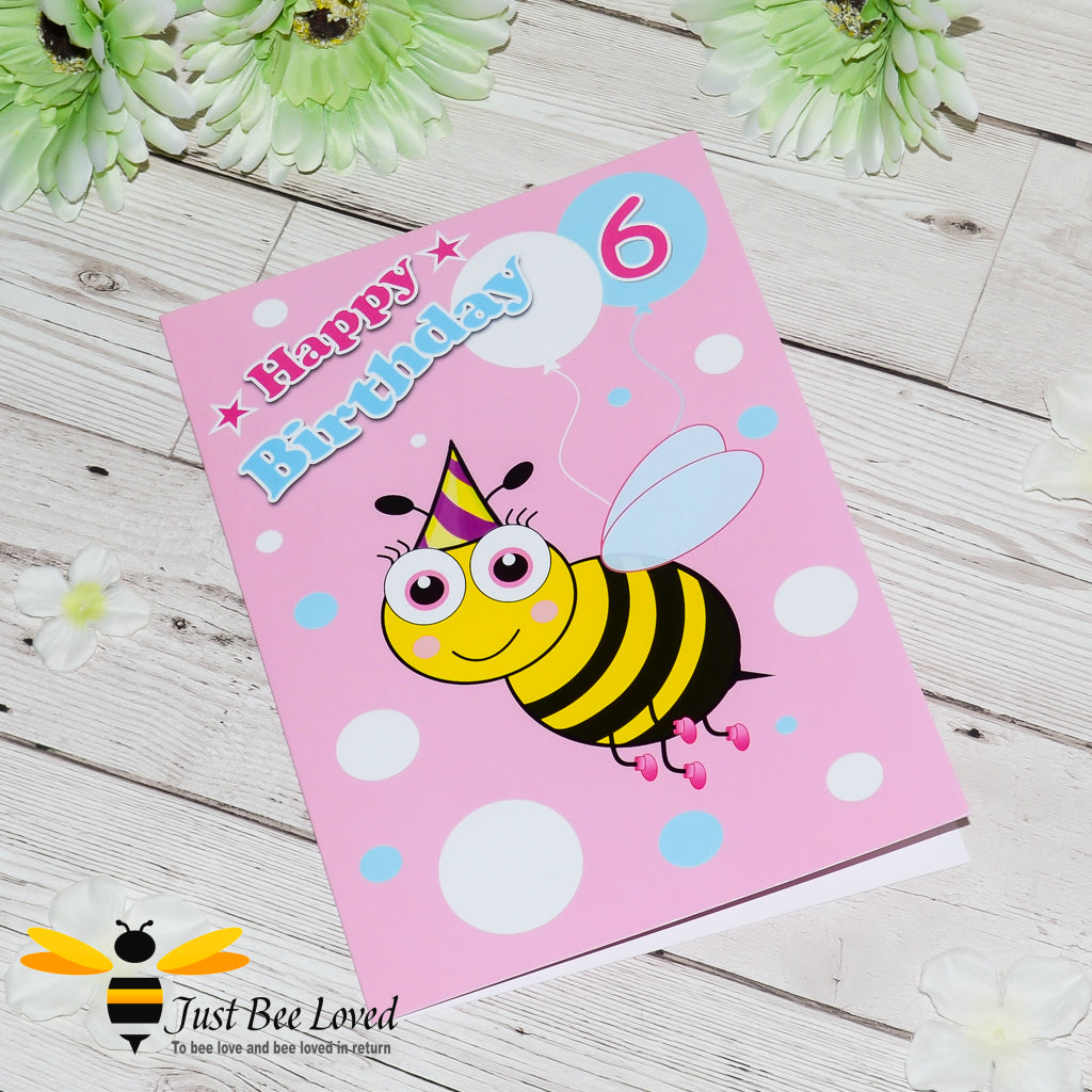 A pink greeting card with a cartoon bee illustration and the text 'Happy Birthday' on the front with the number 6. 