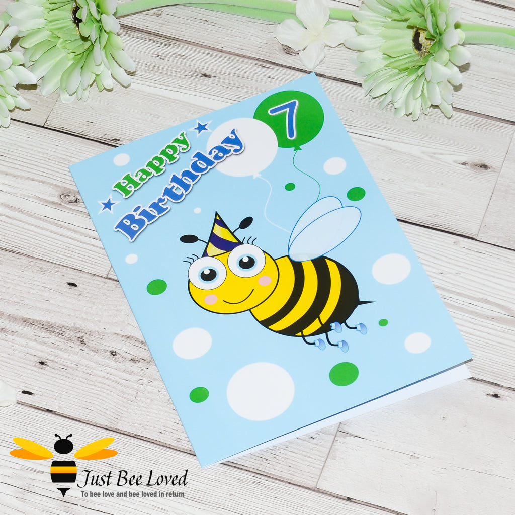 a blue birthday greeting card featuring a cartoon bee wearing a party hat holding a balloon with the number 7.