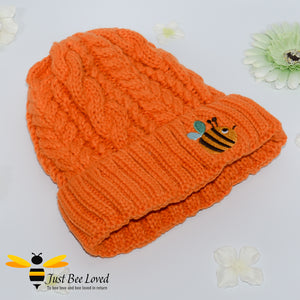 Aran style knitted hat featuring an embroidery bumblebee on front in orange colour