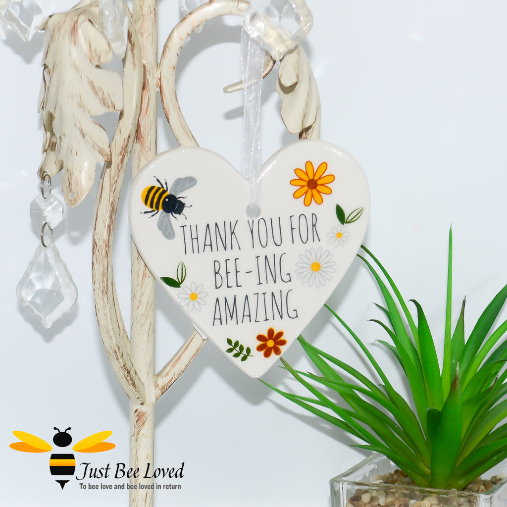a ceramic hanging heart plaque decorated with bees and daisies and "thank you for bee-ing amazing" text.