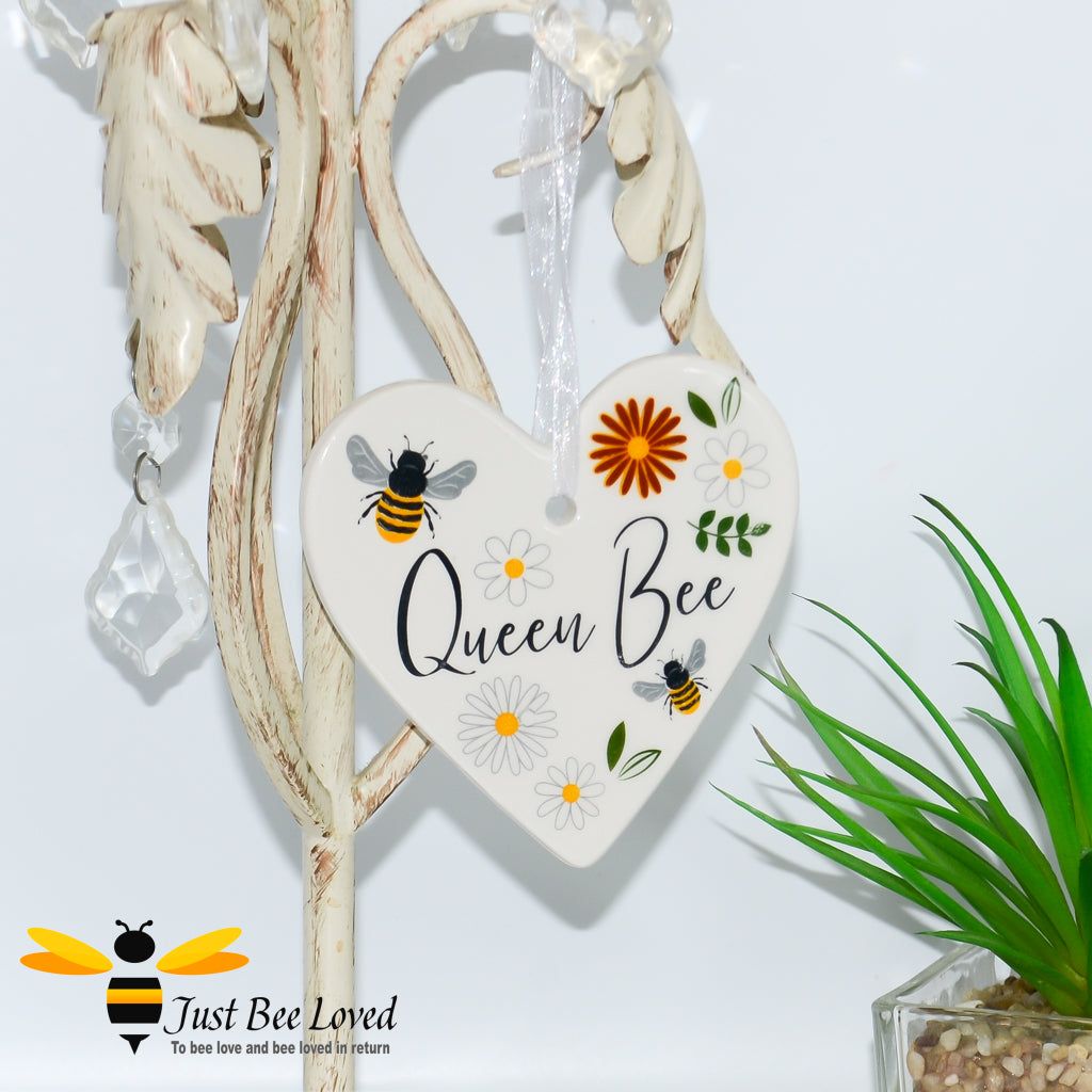 a ceramic hanging heart plaques with bees and daisies and "queen bee" text.