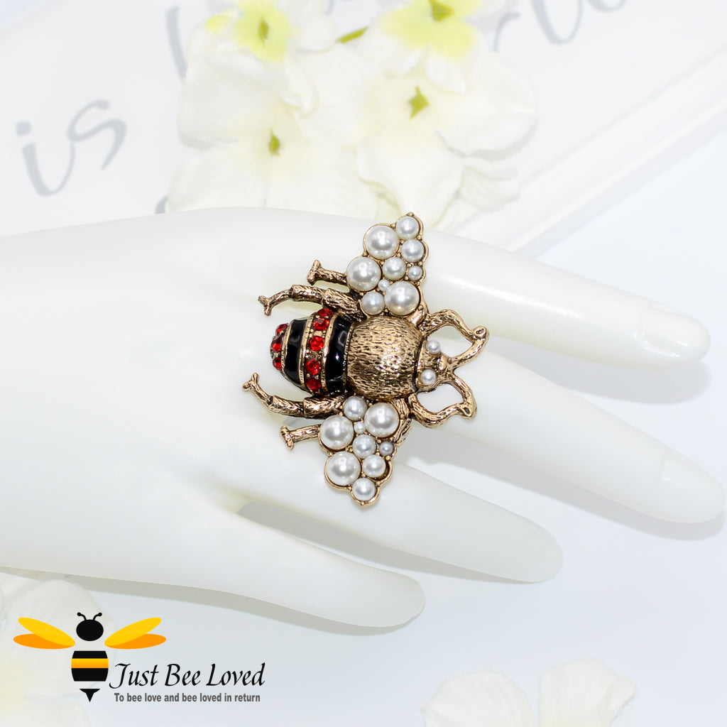 A decorative bee-shaped ring with red rhinestone crystals and white pearls, in aged gold colour.