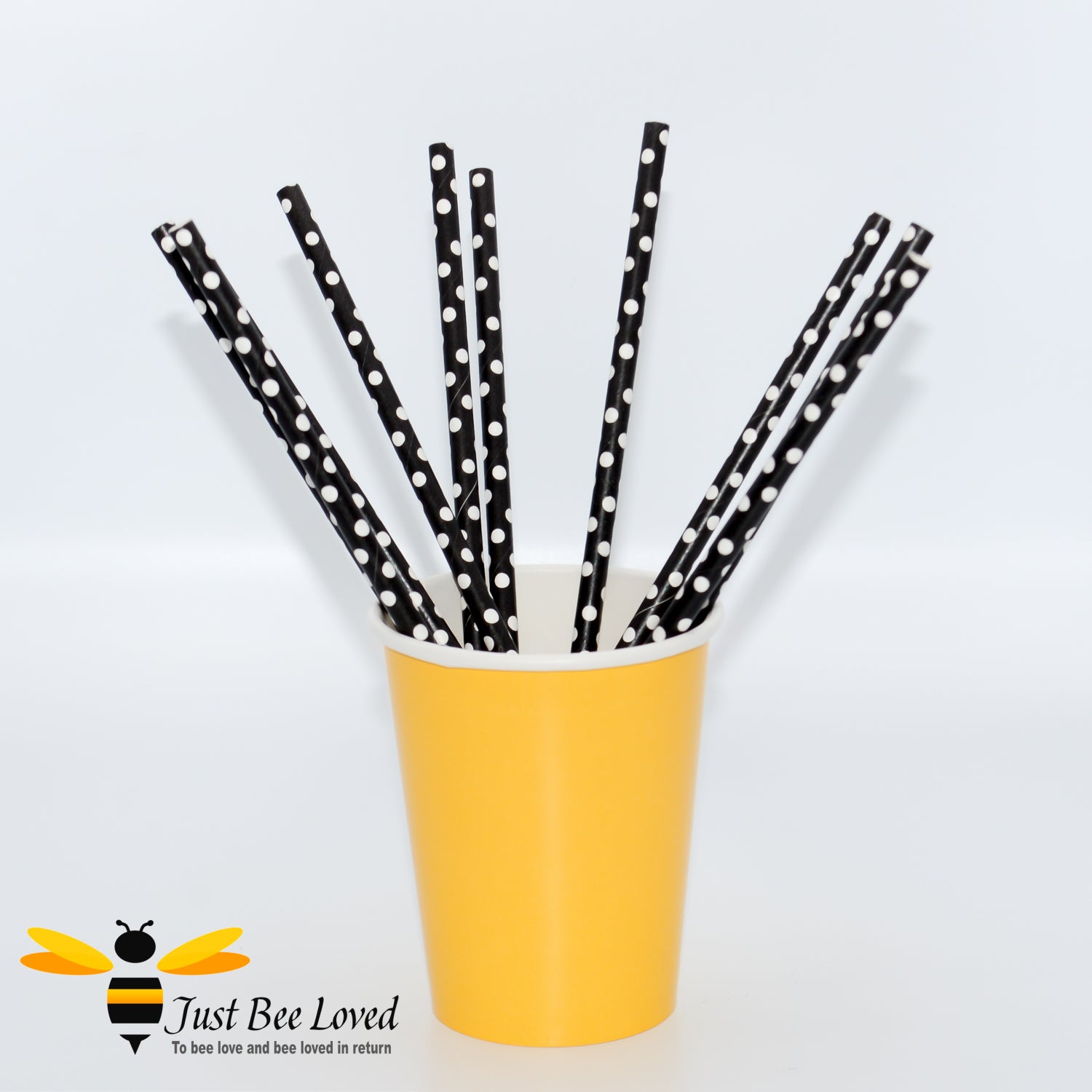 A pack of black and white polka dot paper straws inside a yellow paper cup.