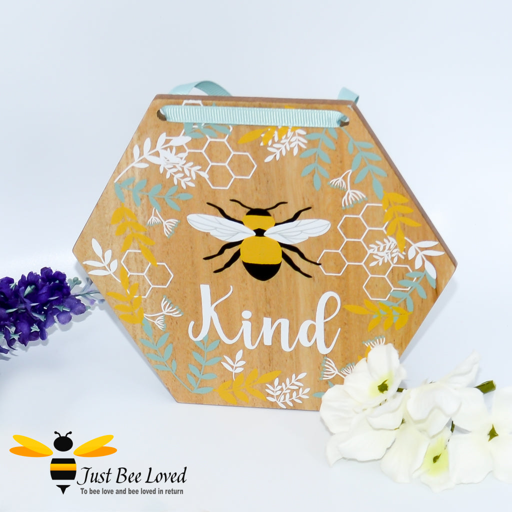 hexagon shaped wooden hanging plaque with a pictorial message 'Bee Kind', decorated with painted honeycomb, blue flowers and matching blue ribbon.