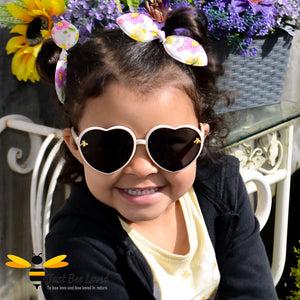 Little girl wearing cream heart shaped bee sunglasses