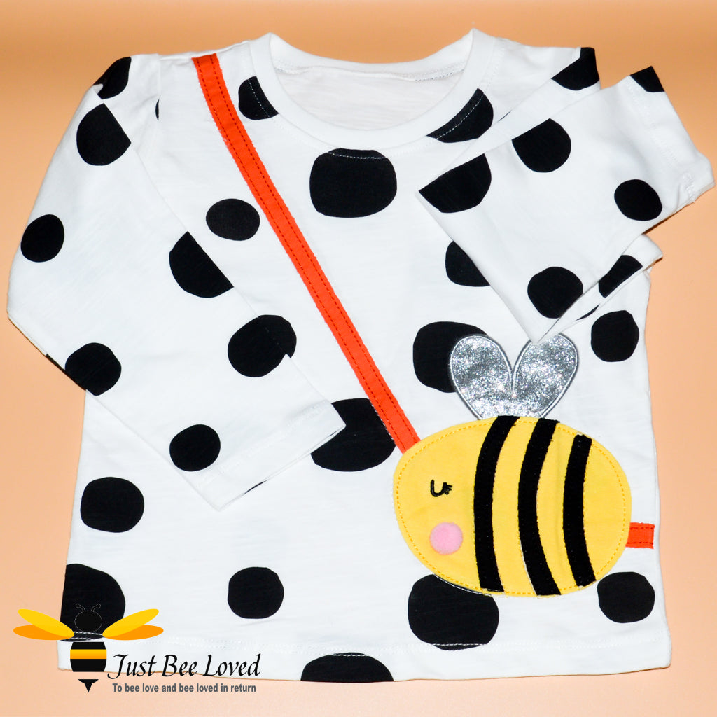 Girl's long sleeve white cotton top featuring multi-sized black polka dots with applique bumblebee handbag design