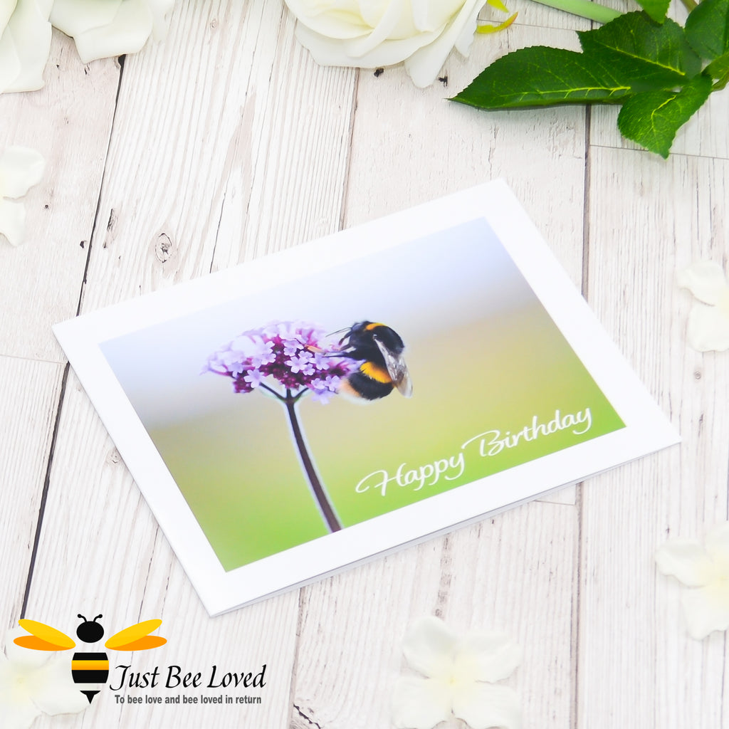 A photographic greeting card depicting a bumblebee foraging on a purple flower with the text 'Happy Birthday'.