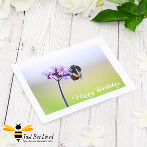 A photographic greeting card depicting a bumblebee foraging on a purple flower with the text 'Happy Birthday'.