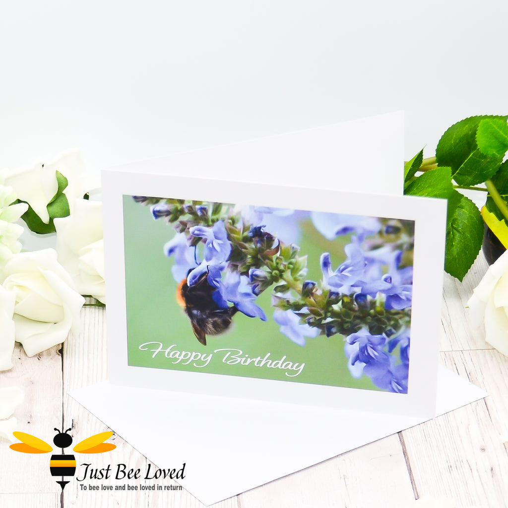 A greeting card featuring a photographic image of a bee drinking nectar from blue salvia flowers with 'Happy Birthday' text.