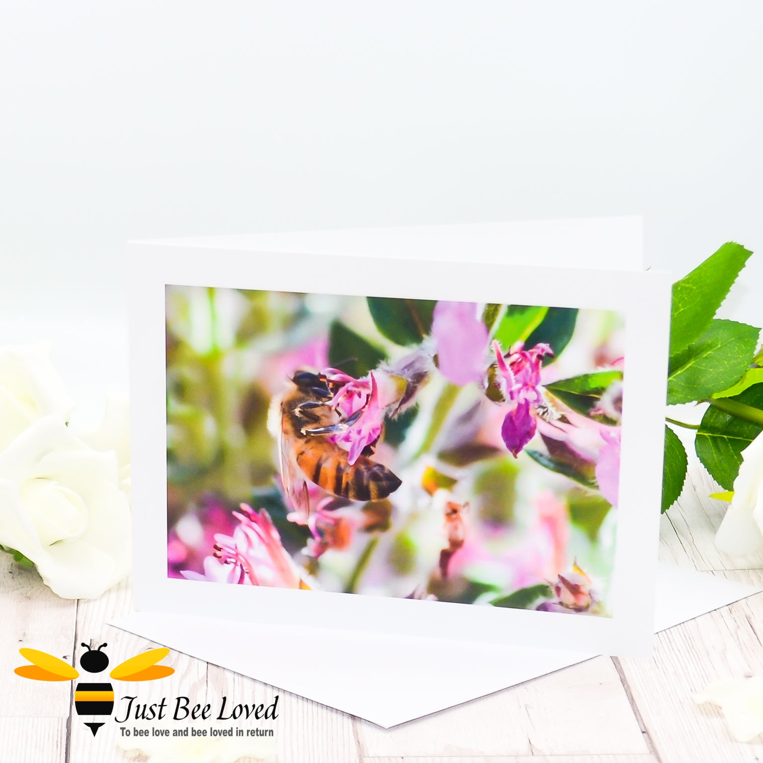 A greeting card featuring an image of a honey bee foraging on wild pink flowers.