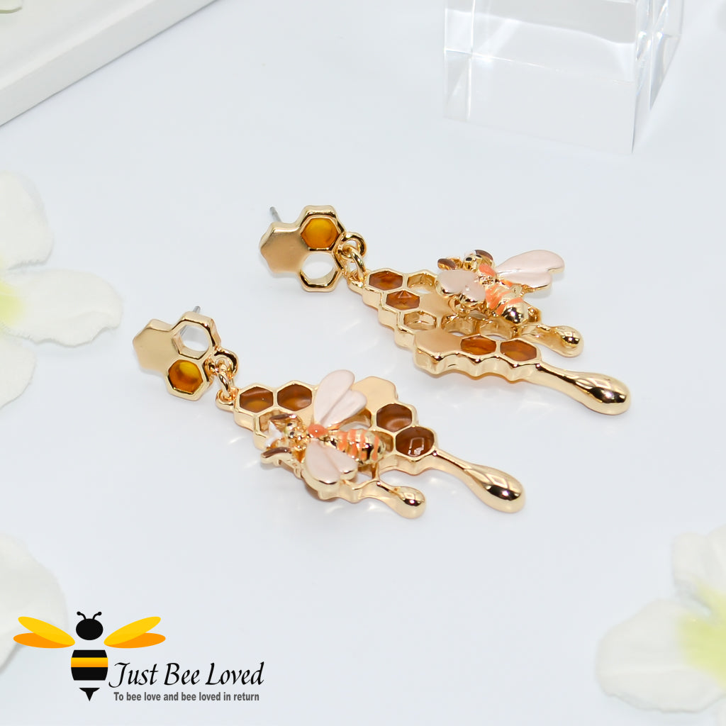 A pair of rose gold metallic drop earrings designed to resemble honey drips and pollen with a honey bee motif