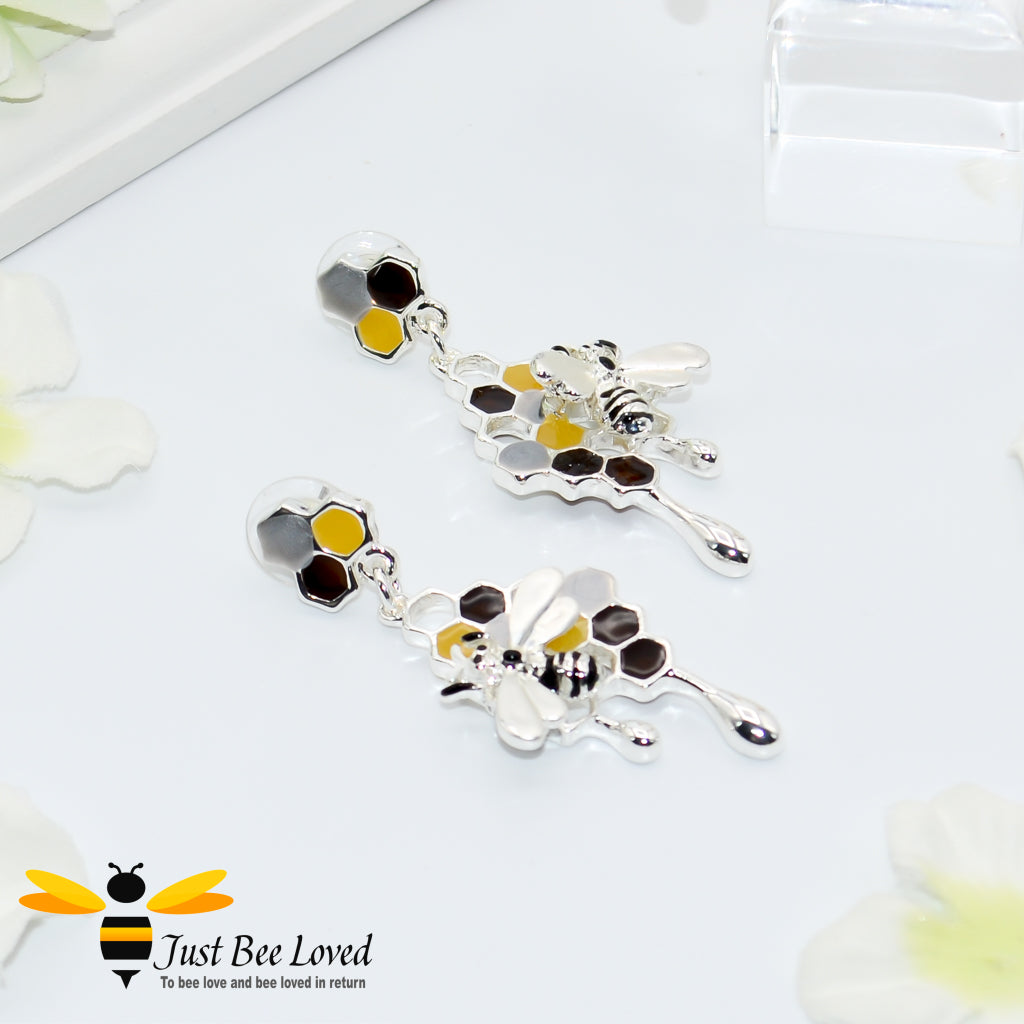 A pair of silver metallic drop earrings designed to resemble honey drips and pollen with a honey bee motif