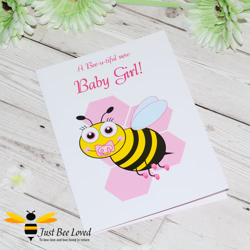 image of a new baby girl newborn bee greeting card featuring a cartoon illustration of a baby bee with a pink dummy and booties, on a honeycomb background.