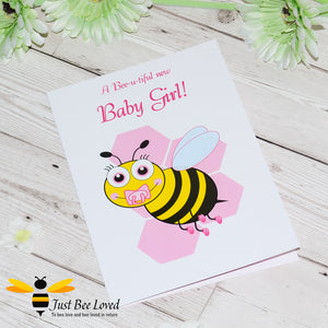 image of a new baby girl newborn bee greeting card featuring a cartoon illustration of a baby bee with a pink dummy and booties, on a honeycomb background.
