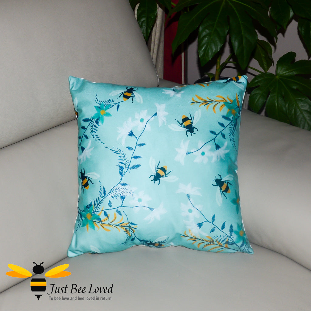 Teal coloured scatter cushion featuring an embroidery design of foraging bees and flowers.