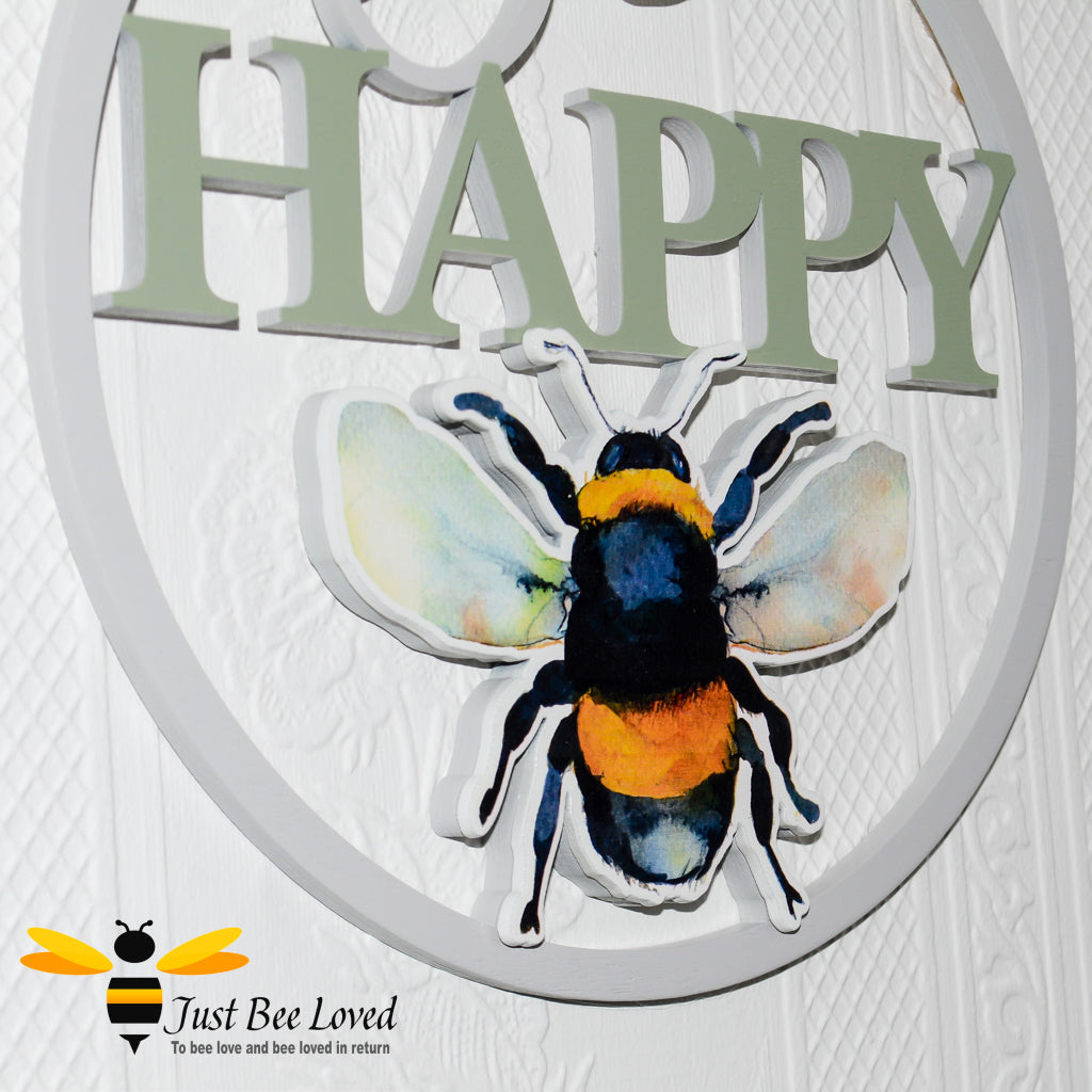 A wooden round hanging plaque with a cut out silhouette of a bumblebee and the message 'Bee Happy'.