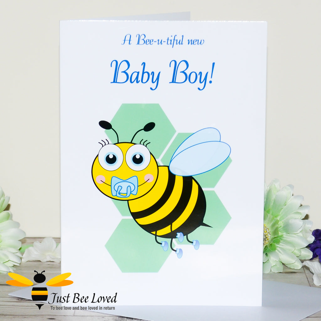 a newborn baby boy bee card featuring a cartoon illustration of a baby bee with a blue dummy and booties on a honeycomb background.