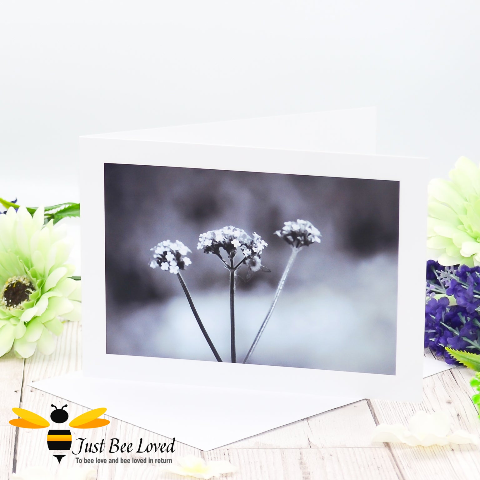 a photographic greeting card featuring a black and white image of a bee on a misty morning with flowers, presented with a white envelope.
