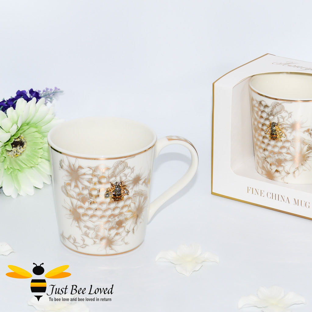 An ivory fine China mug decorated with golden honeycomb, flowers, with a rhinestone bee embellishment and gold rim, presented alongside a gift box.