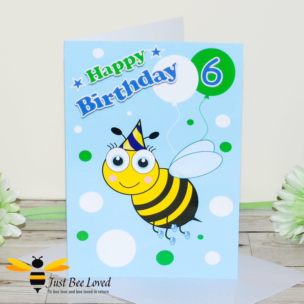 a birthday greeting card for a boy featuring a cartoon bee wearing a party hat, colourful balloons and the number 6.