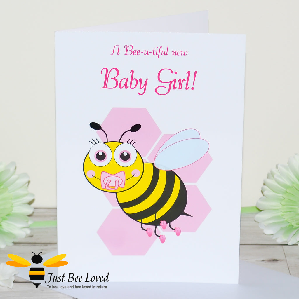 a newborn baby girl bee card featuring a cartoon illustration of a baby bee with a pink dummy and booties, on a honeycomb background.