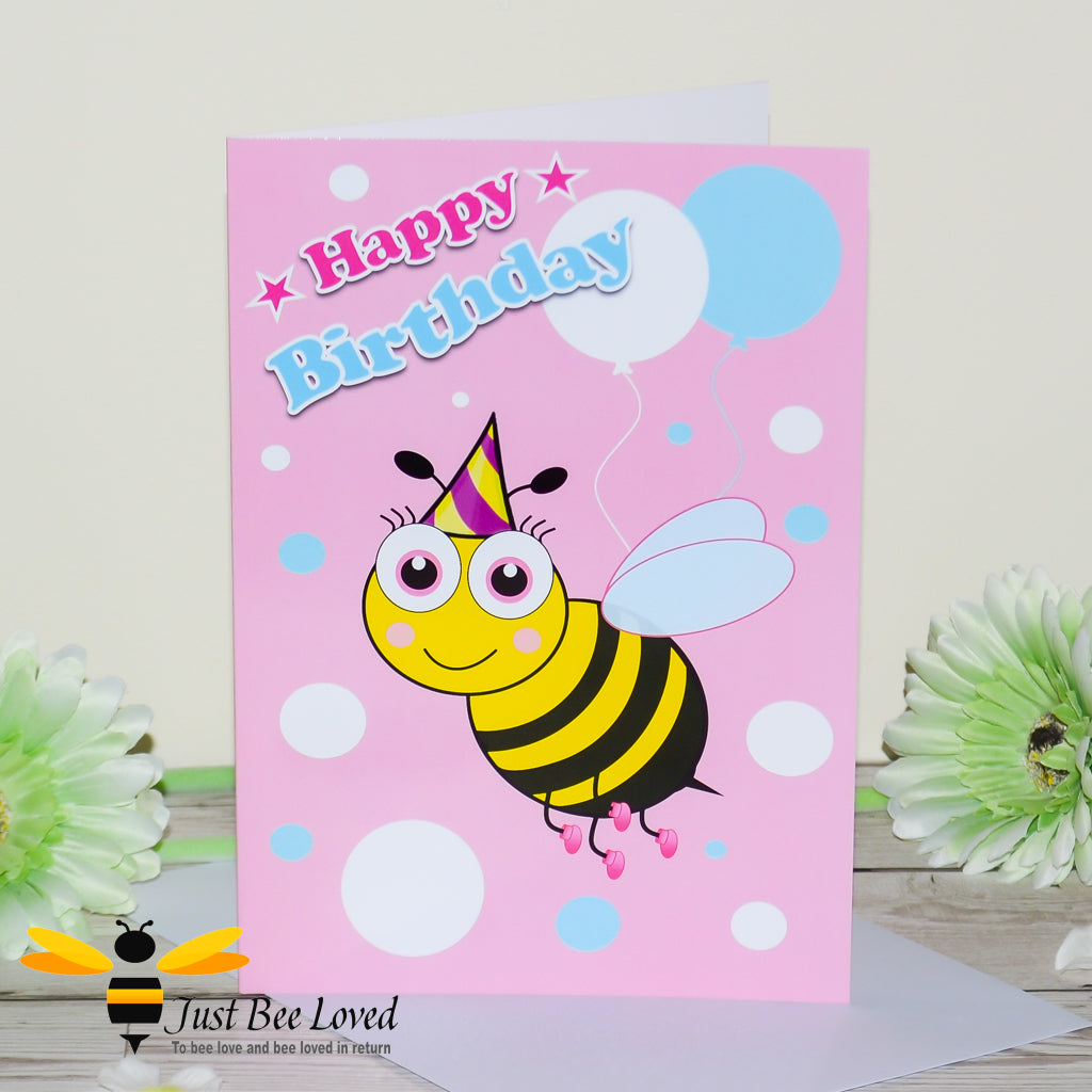 a pink birthday bee card with a cartoon illustration of a toddler bee wearing a pink hat and holding colourful balloons.